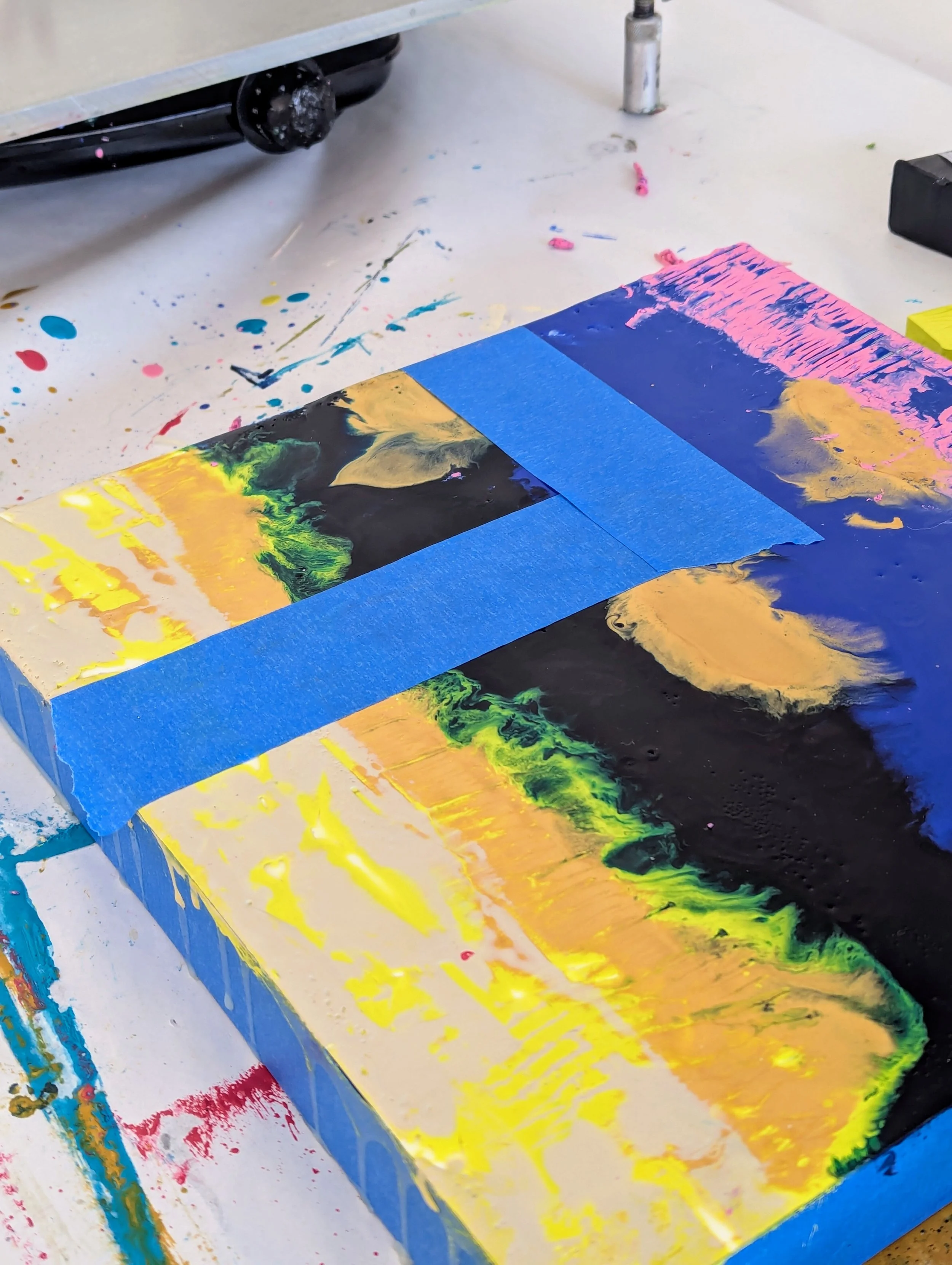 Abstract acrylic painting on a canvas with black, blue, yellow, pink, and green colors, taped with blue painter's tape.