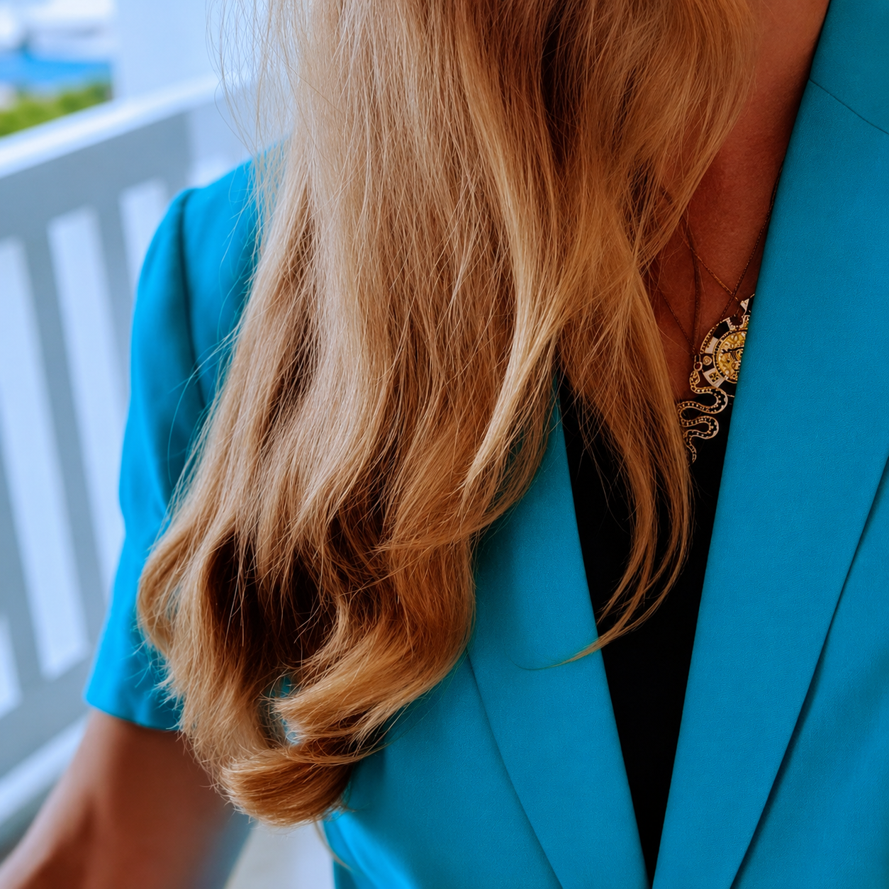 Close-up of a woman with long, wavy, blonde hair wearing a turquoise coat and a necklace.