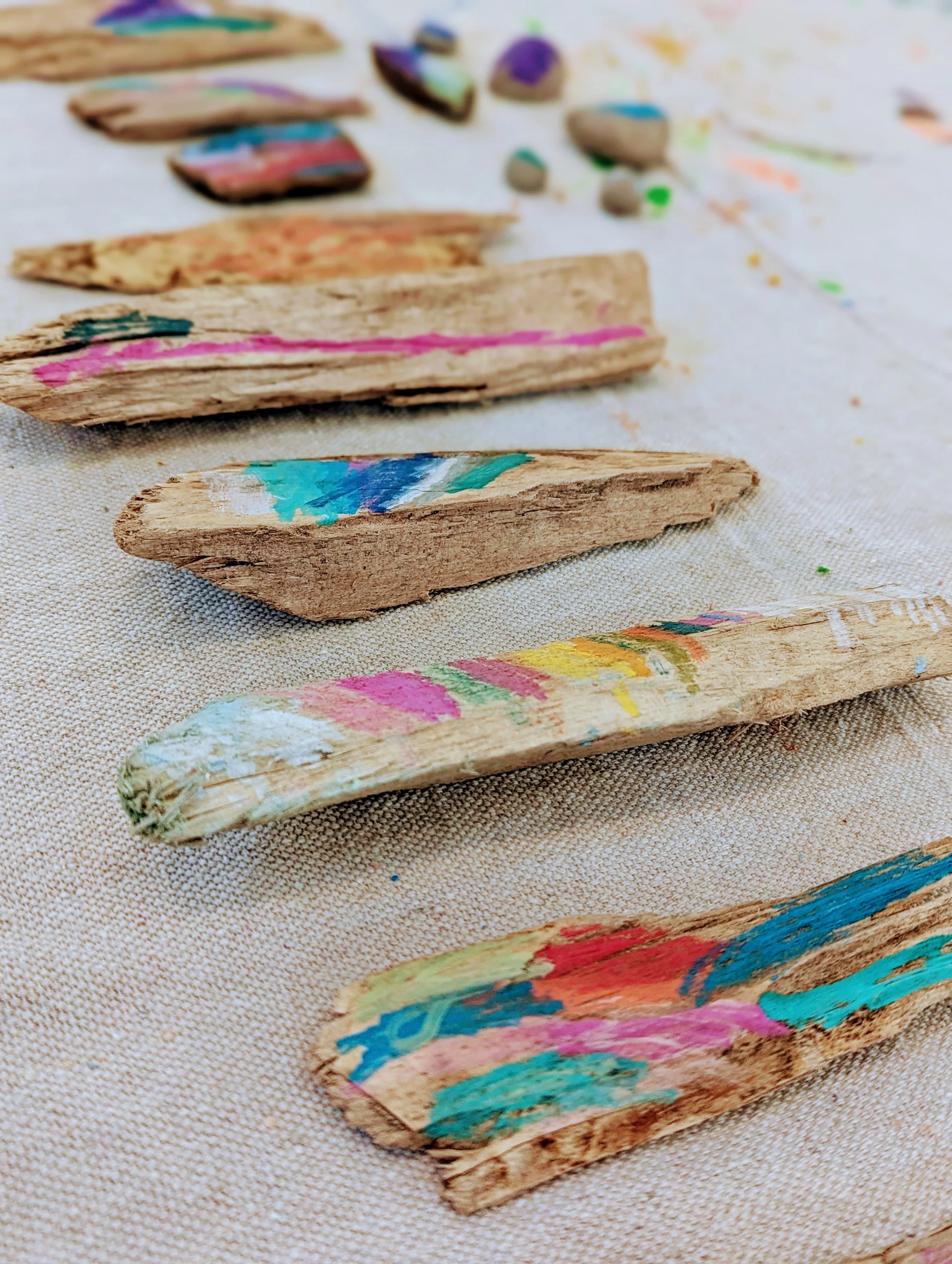 Painted and colorful broken pieces of wood or bark arranged on a textured surface, with various colors and brushstrokes.
