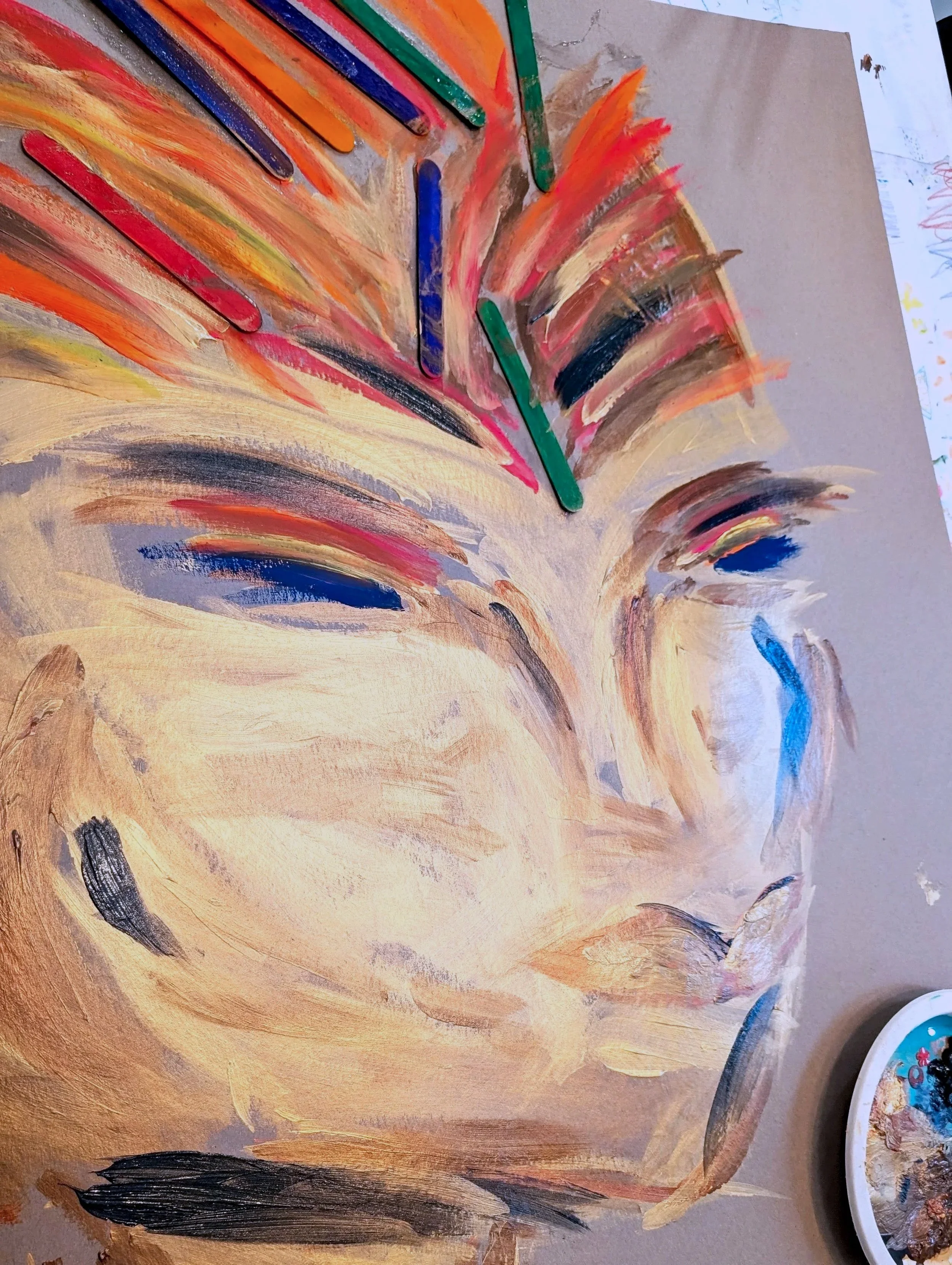 Close-up of a painted open book with colorful brush strokes and painted popsicle sticks attached, creating an abstract art piece.