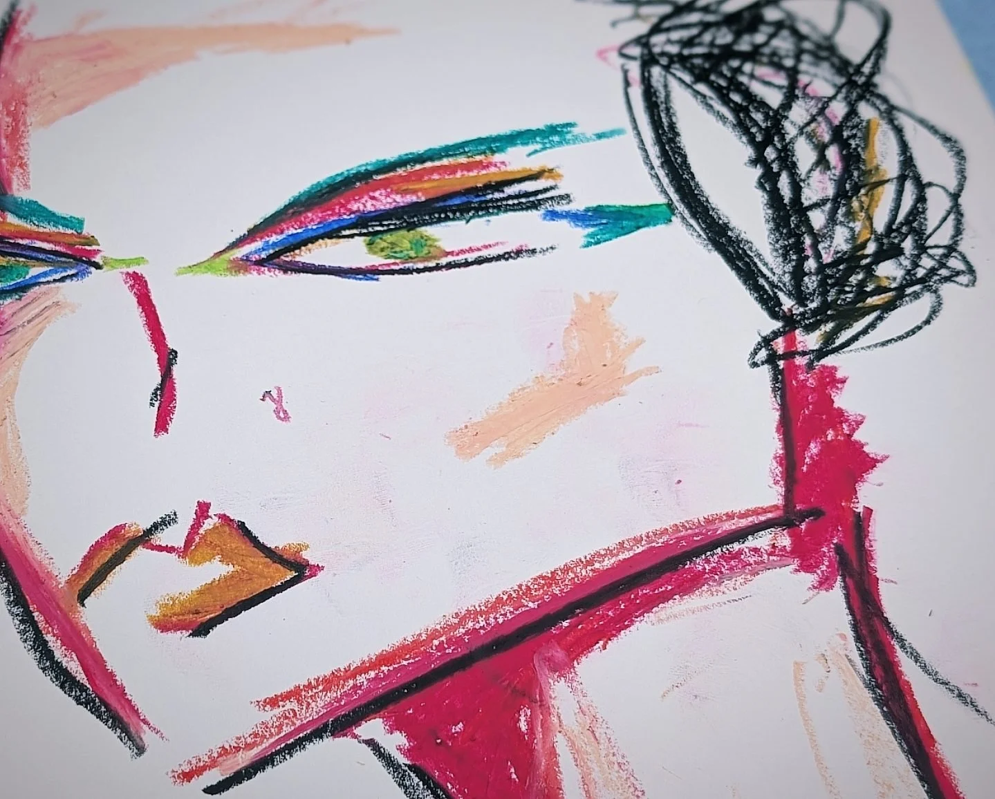 Child's drawing with colorful crayons on white paper, featuring a face with multicolored eye and hair and a black scribble on the right.
