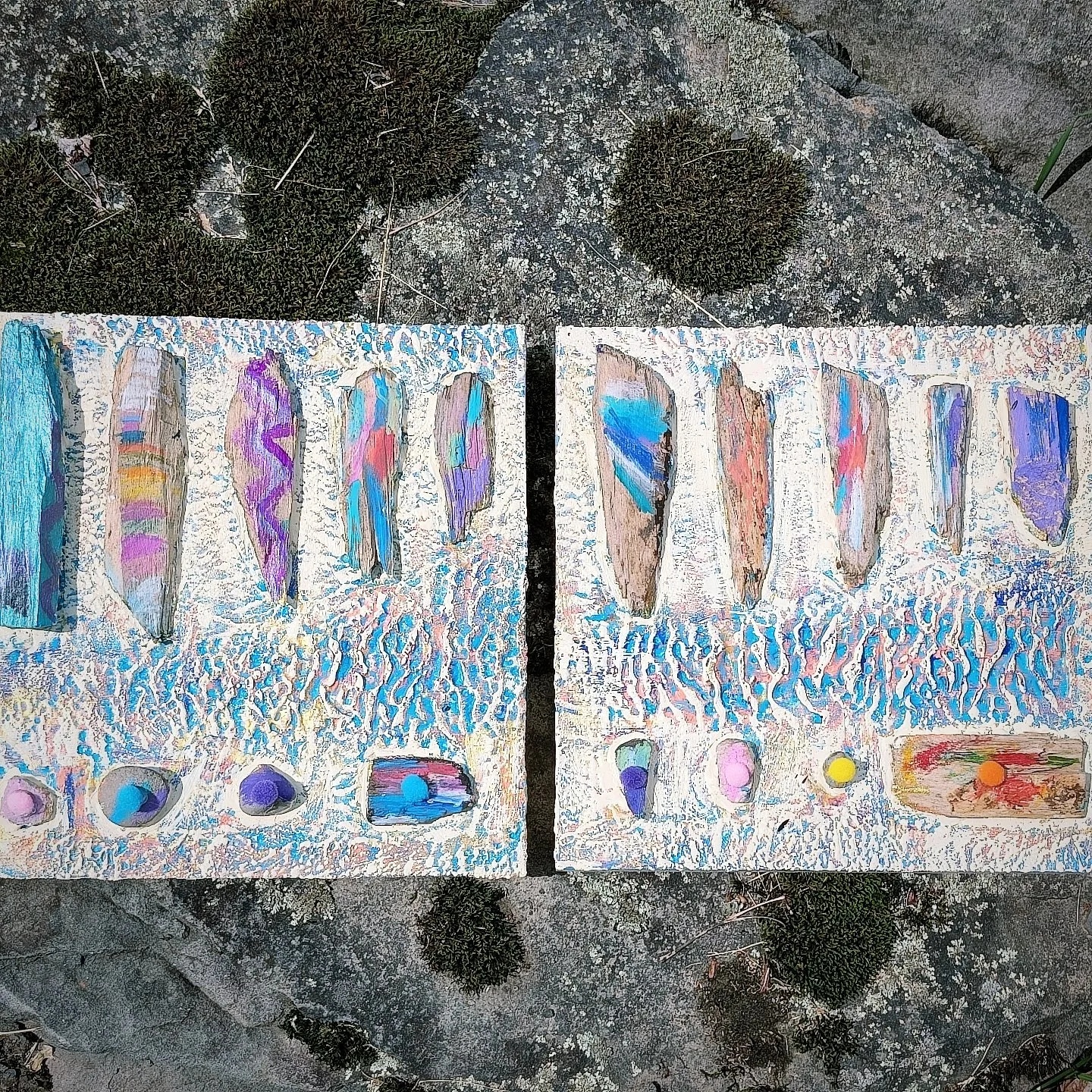 Two painted rocks with colorful designs, placed on a textured white surface, outdoors with rocks and moss in the background.