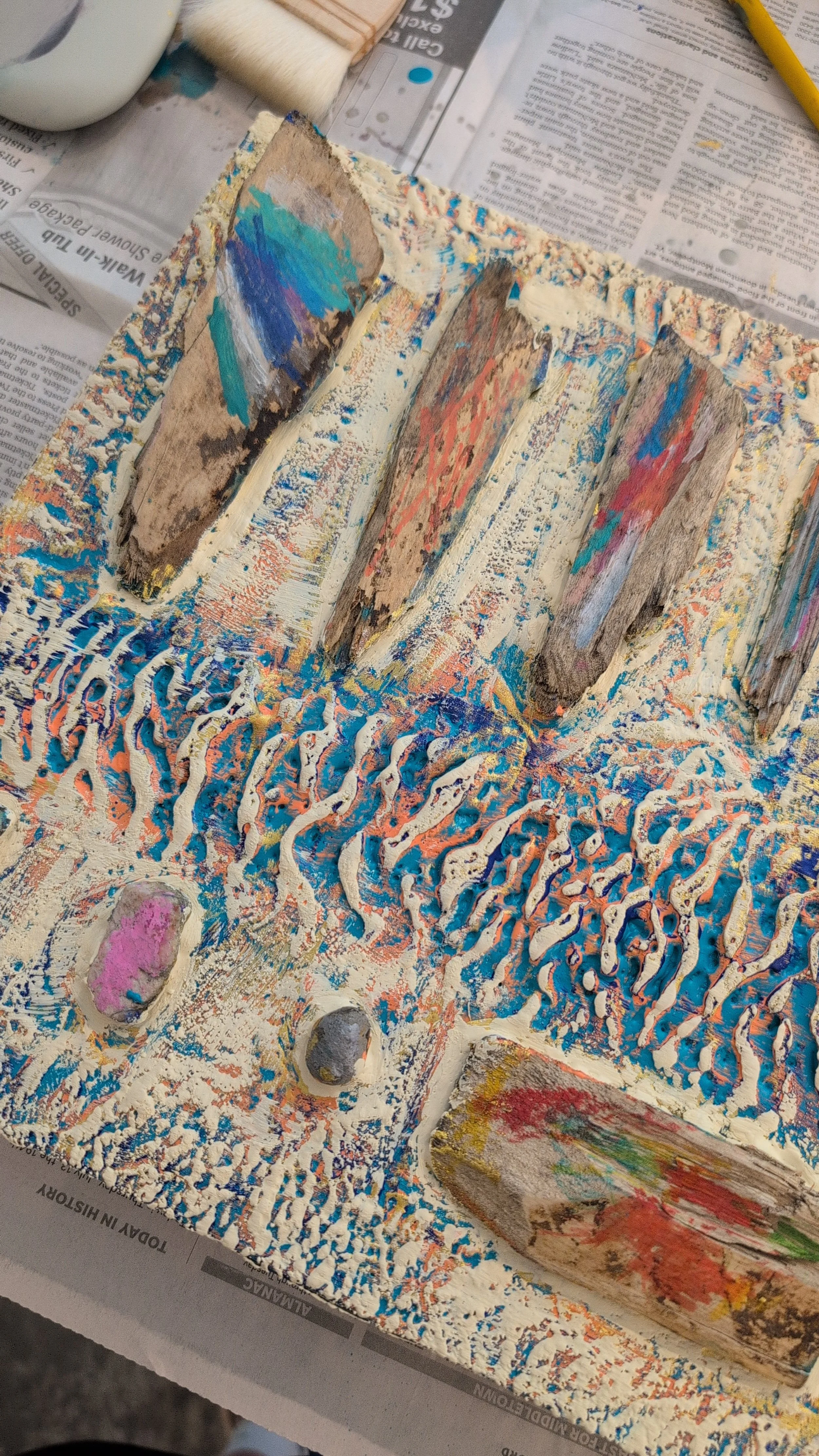 A paint palette with multiple layers of dried paint, colorful smears, and textured patterns, resting on a newspaper-covered surface.
