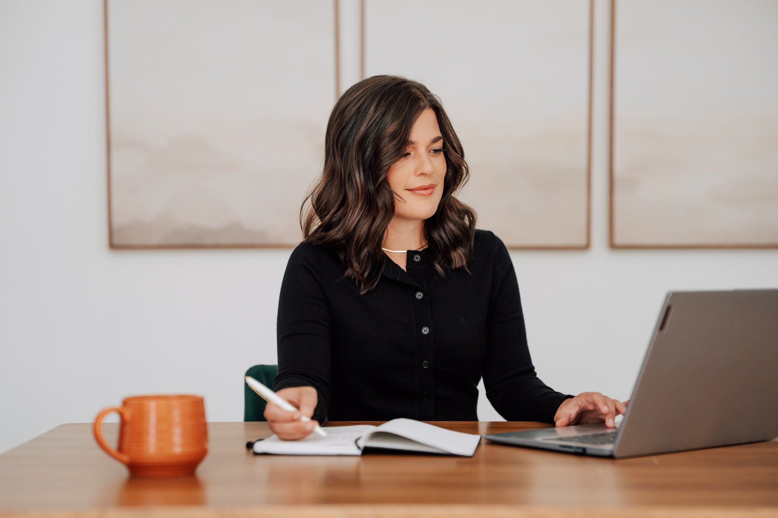 Founder of Alpine Virtual Assistants working at a desk with a laptop and notebook, providing virtual assistant and business support services.