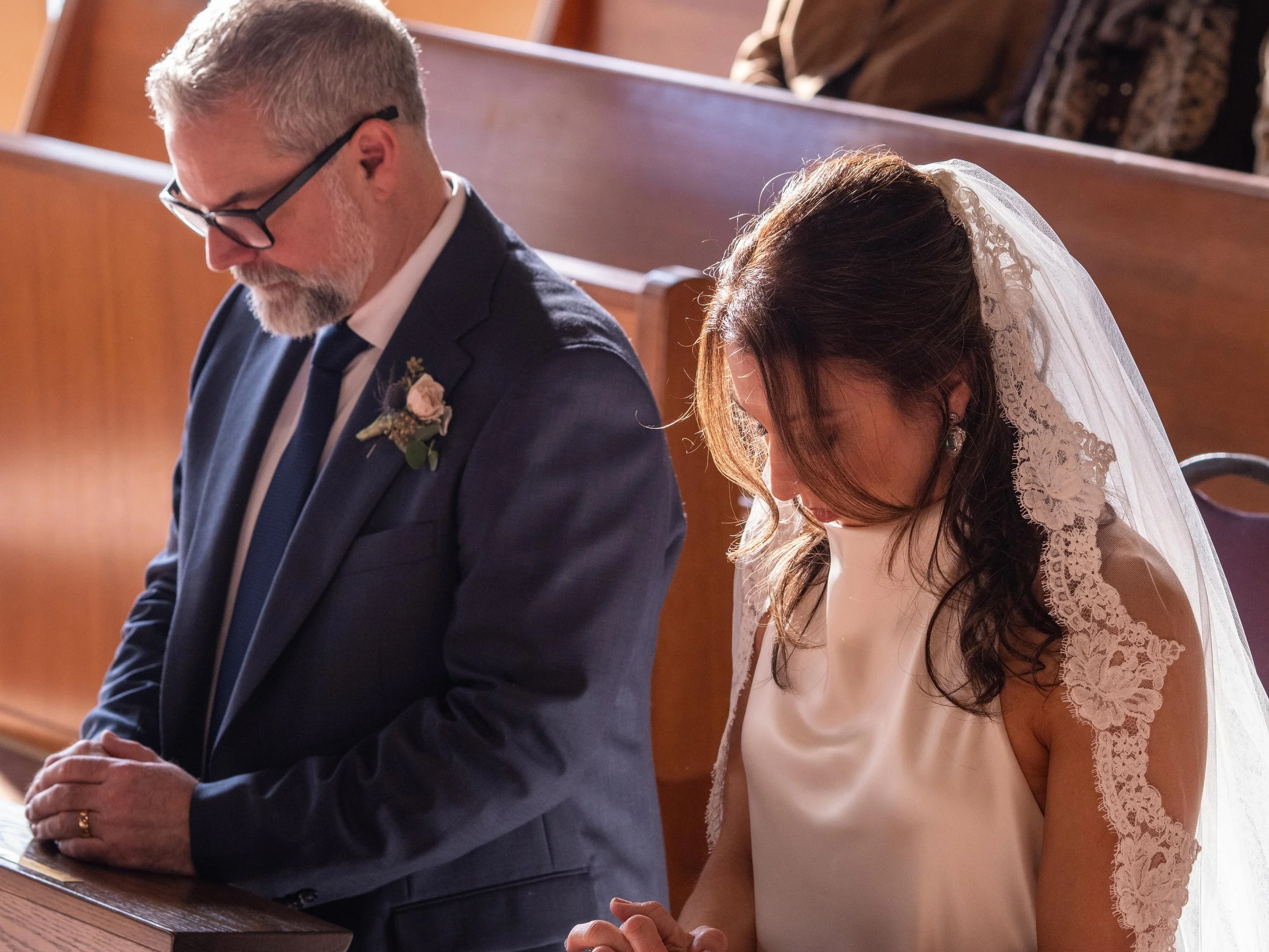A bride and groom praying with heads bowed during their wedding ceremony inside a church.