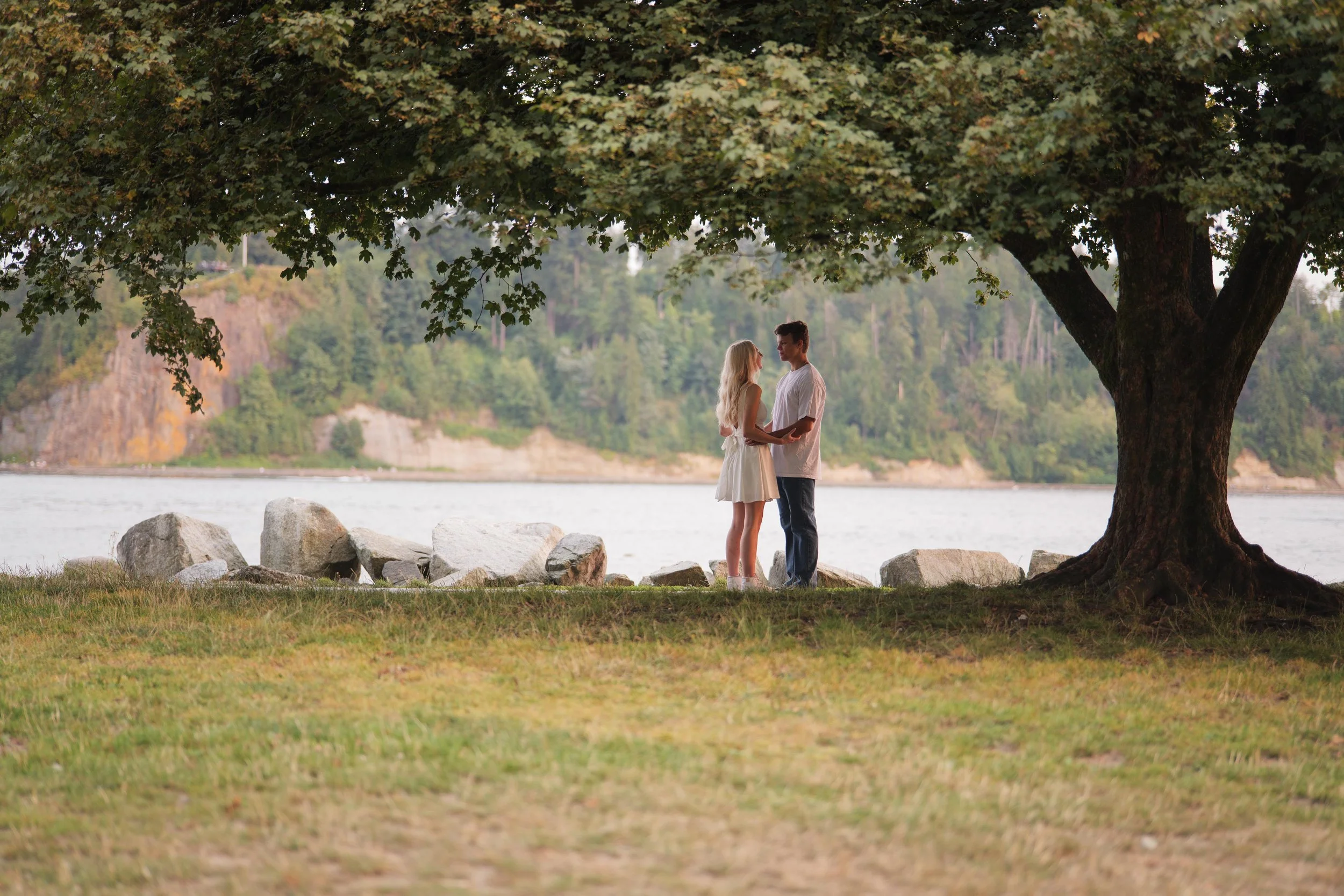 Kiarrah and Julian facing each other beneath a tree during their West Vancouver engagement photography session.