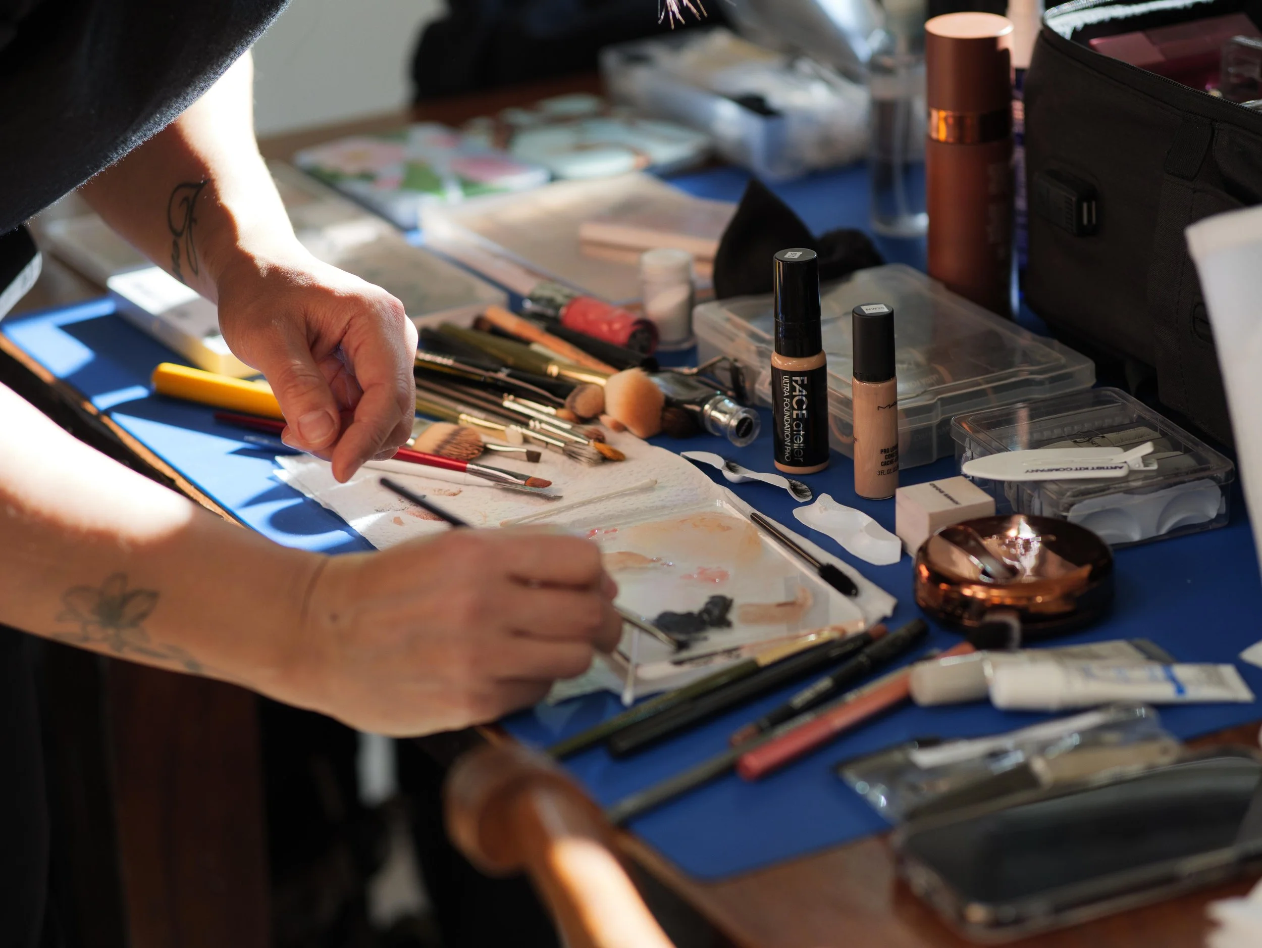 Person's hands arranging makeup brushes and tools on a blue table with various makeup products and accessories.