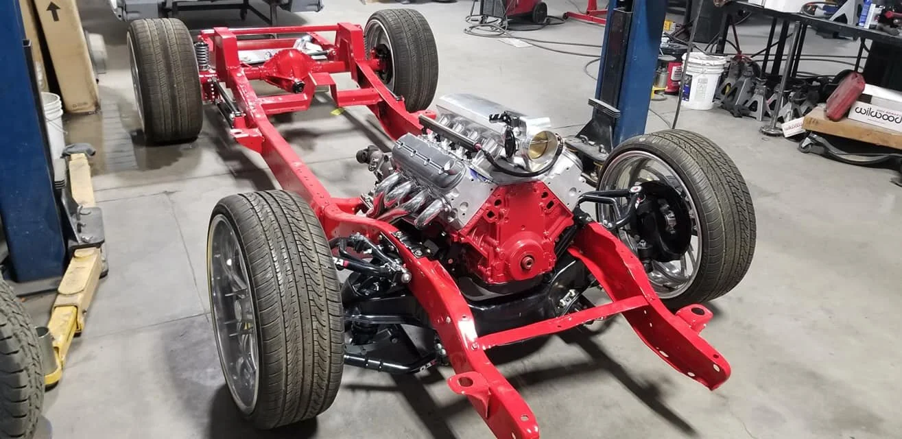 Red car chassis with engine and wheels in a workshop environment.