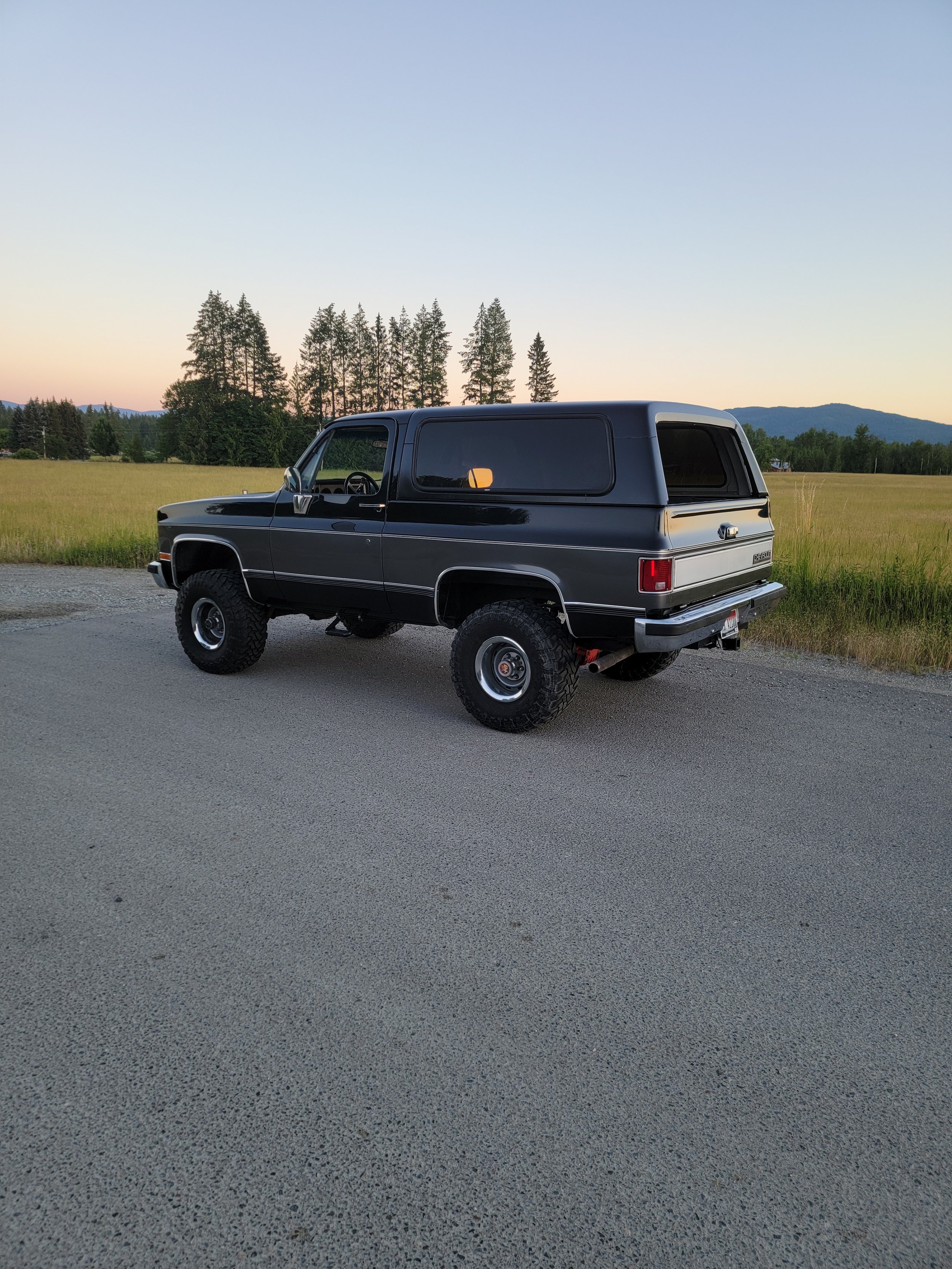 Black SUV parked on a road with a field and trees in the background during sunset.
