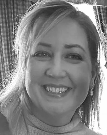 A smiling woman with shoulder-length hair in a casual setting.