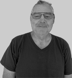A man with short gray hair, wearing glasses and a black t-shirt, smiling at the camera.