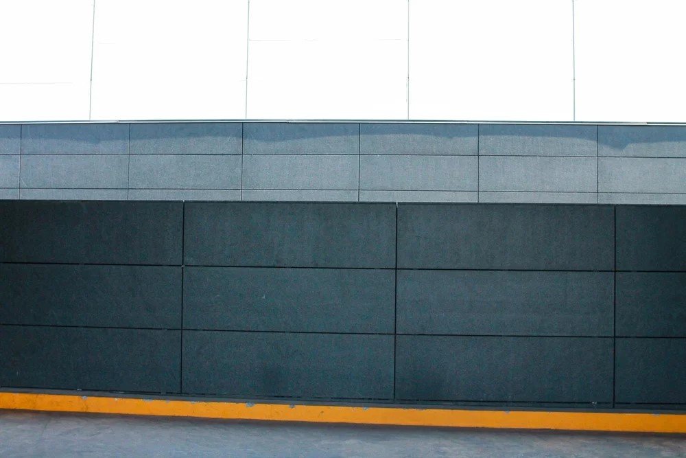 Close-up of a modern building with gray and white exterior panels and a yellow curb at the bottom.