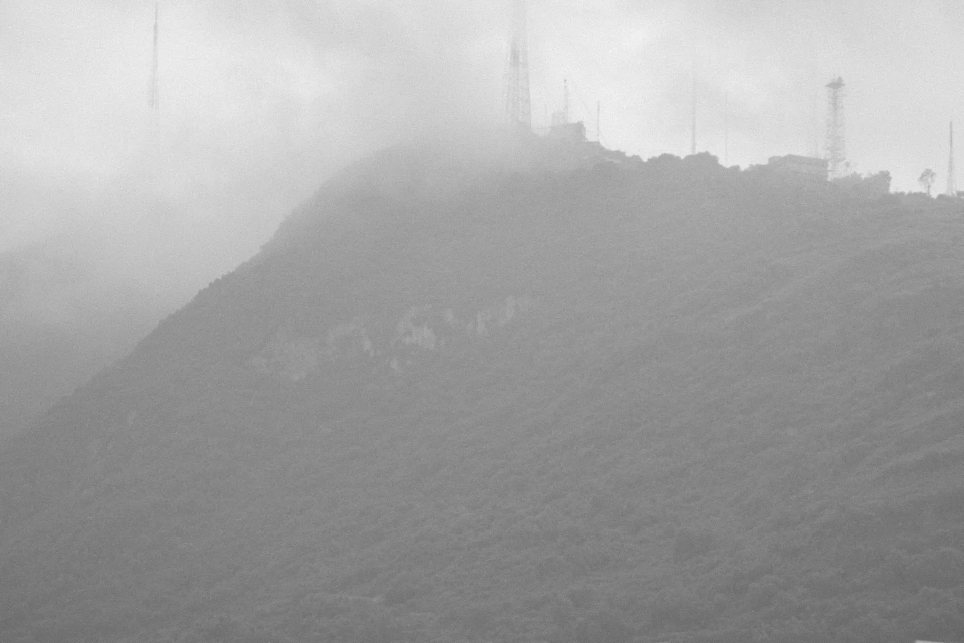A foggy landscape of a hilly area with communication towers and trees in the background.