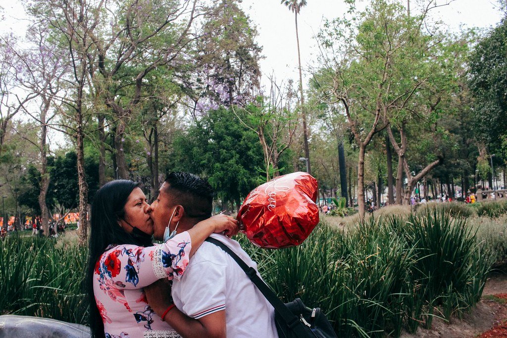 A couple kissing outdoors in a park, with the woman holding a heart-shaped red balloon.