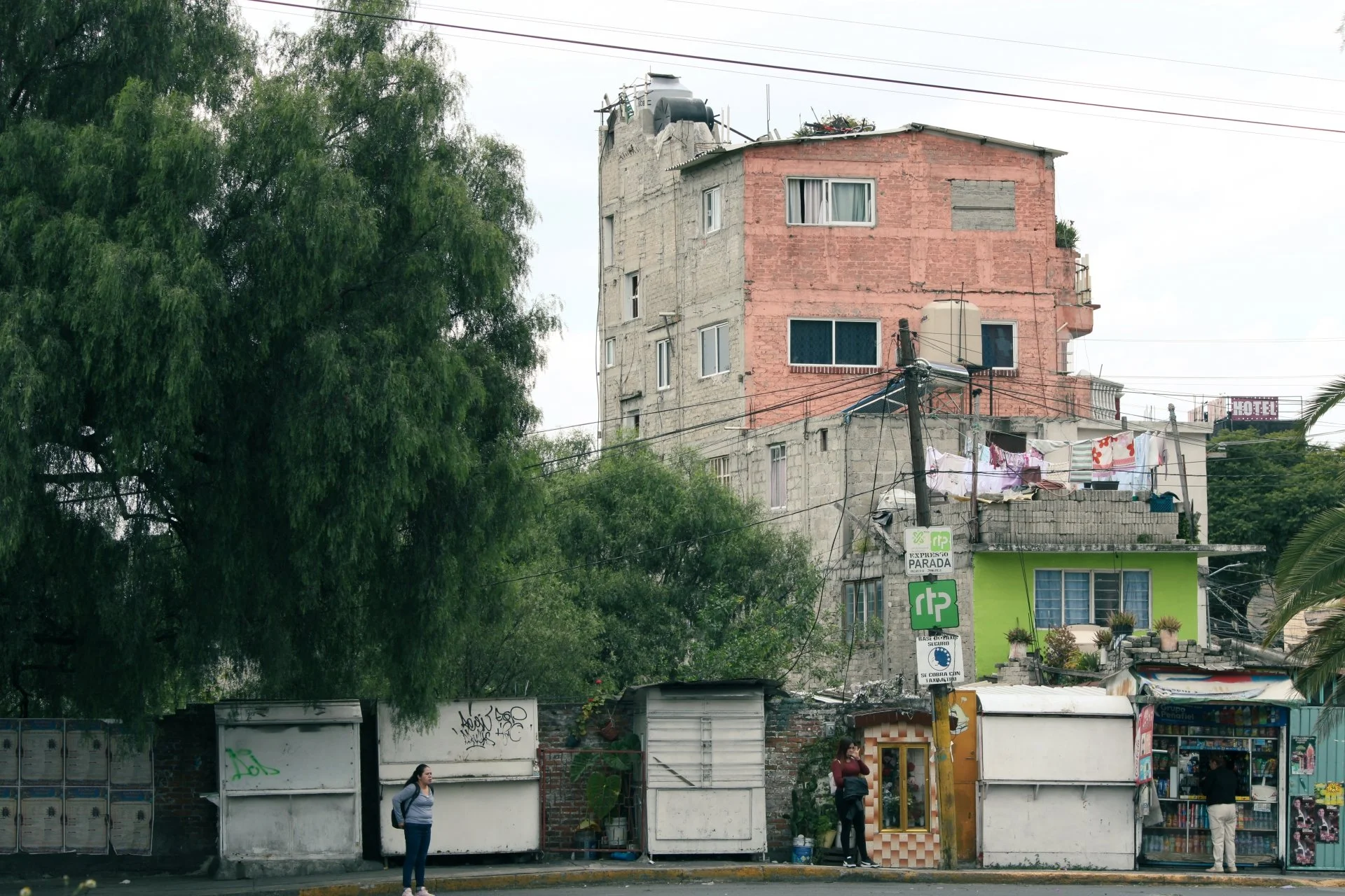Street scene with a small marketplace in front of residential buildings, trees, and a signboard with safety and health notices.