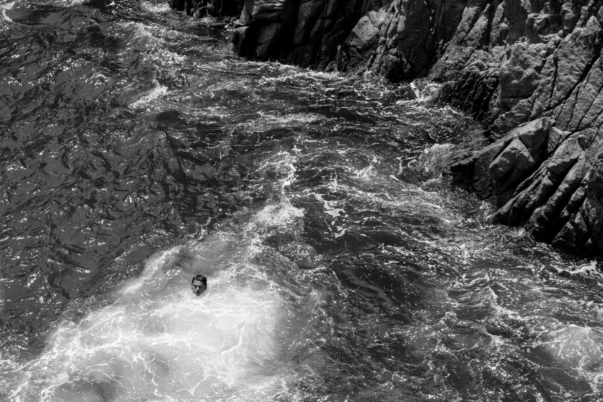 A person swimming in a body of water near rocky cliffs.
