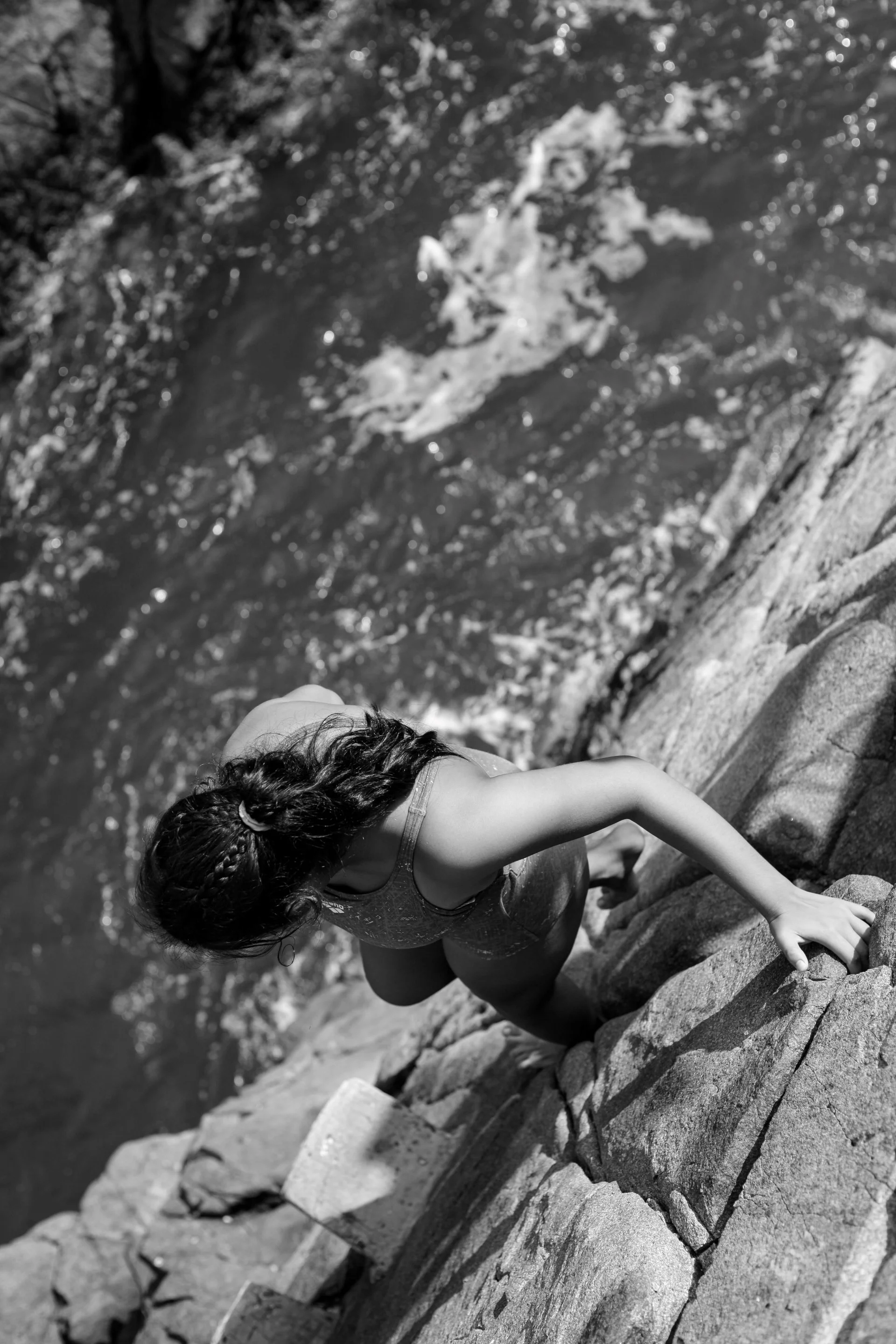 A person climbing rocks along a riverbank, with water and trees in the background.