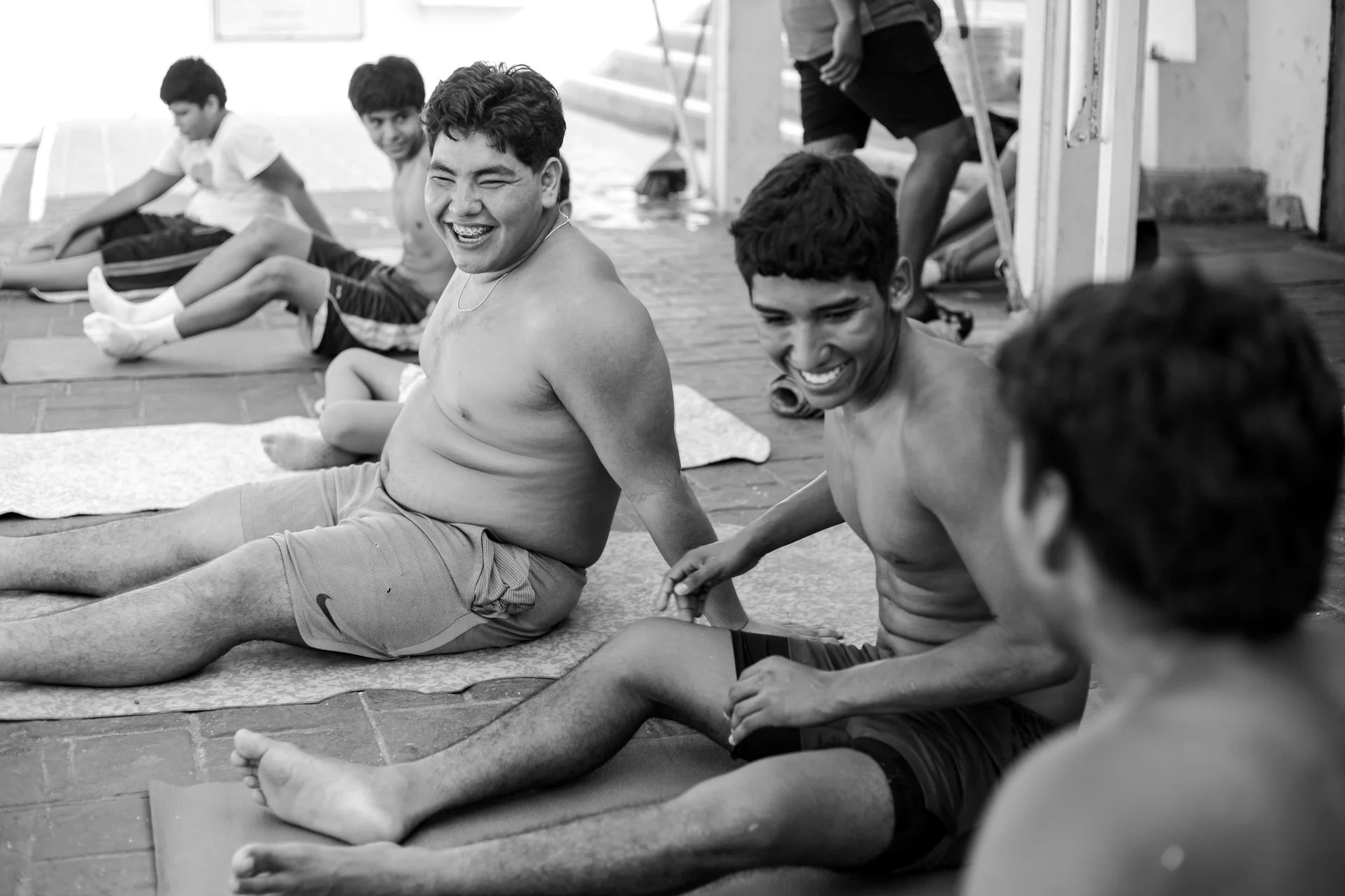 A group of boys sitting on yoga mats against a wall, smiling and talking during a yoga class.