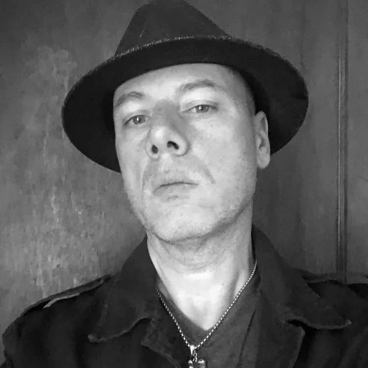 Black and white portrait of a man wearing a fedora hat and a dark shirt.
