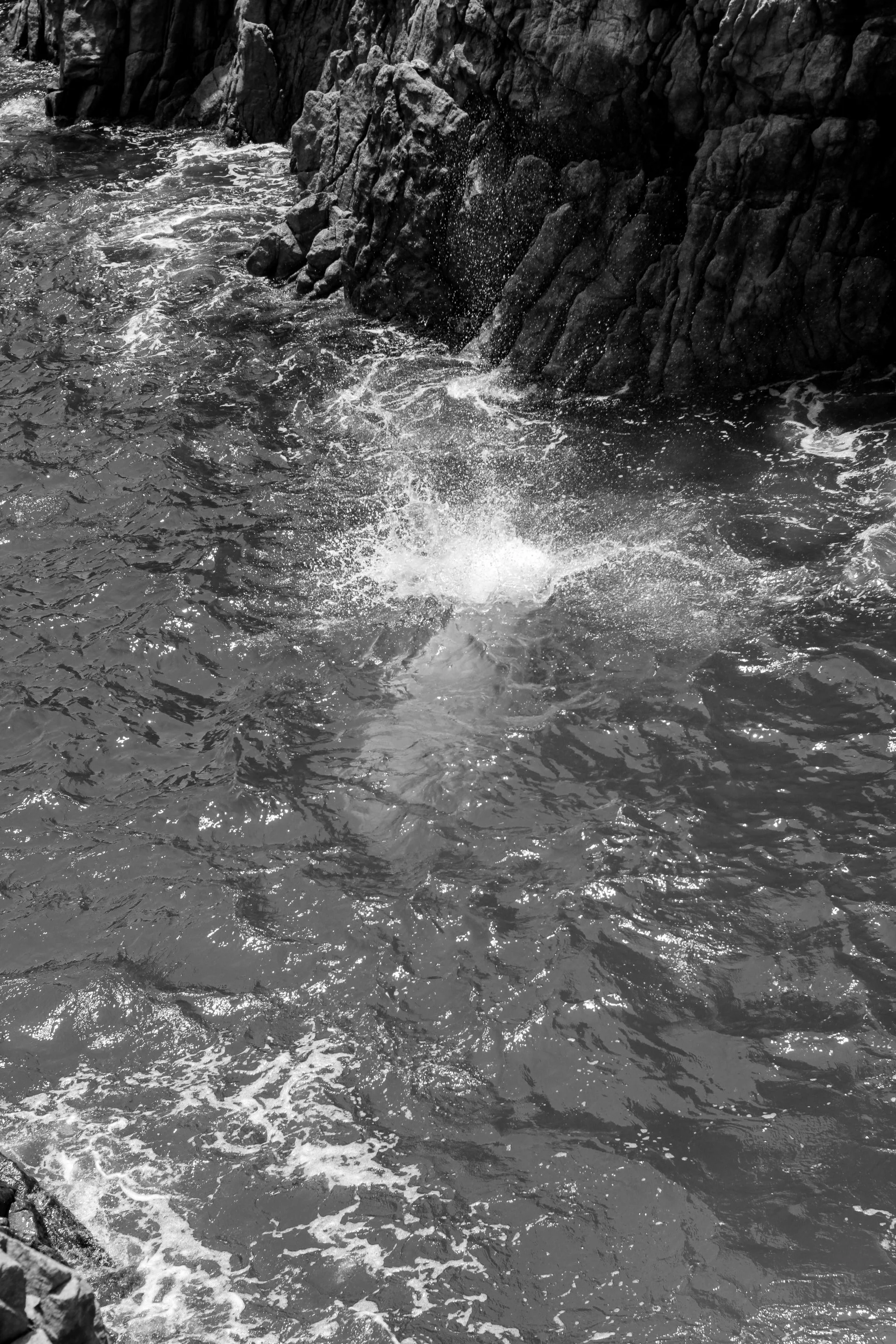 Black and white photo of water splashing against rocks along a shoreline.