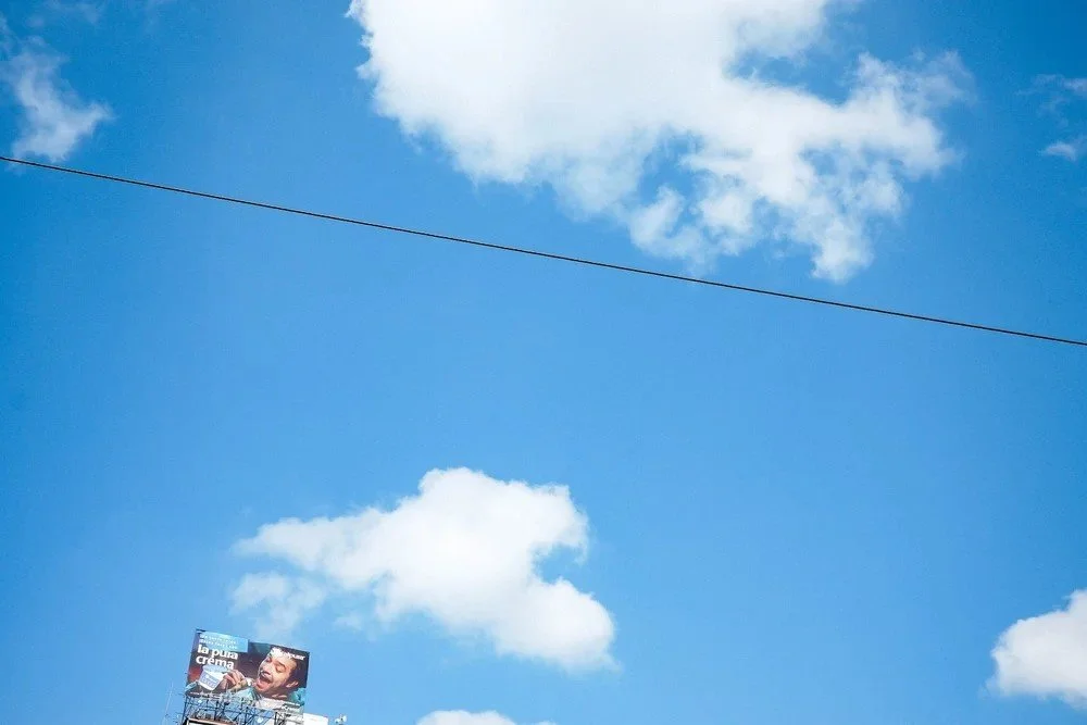Blue sky with white clouds and a billboard showing a man singing into a microphone.