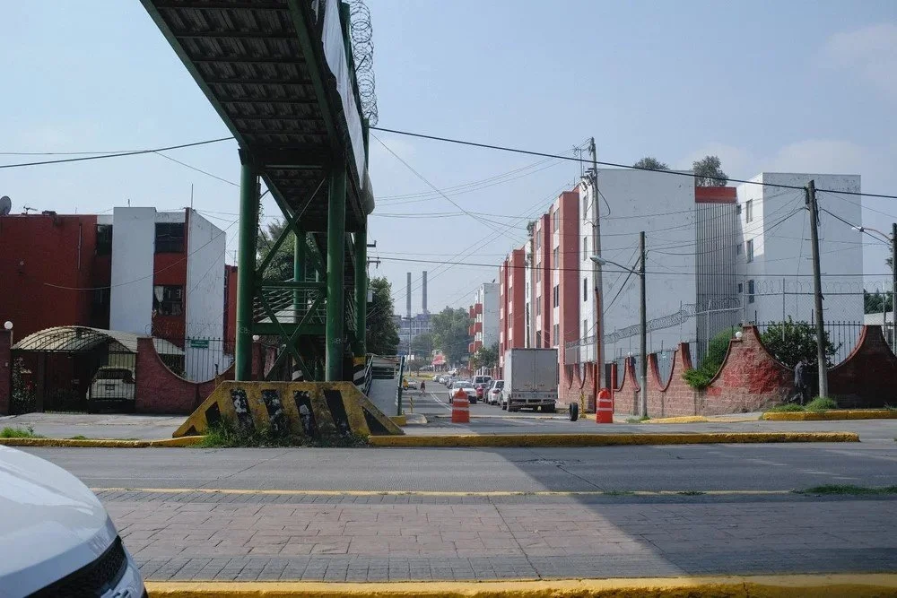 Urban street scene with a highway overpass, some cars, a white truck, and red-brick buildings on a sunny day.