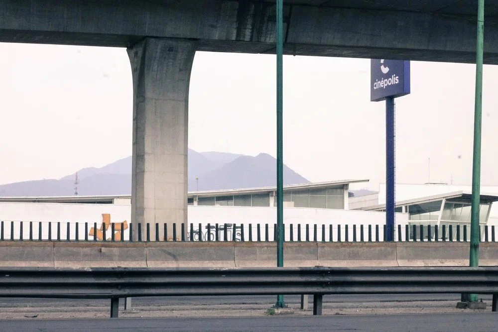 Under an overpass, a Cinepolis sign, some distant mountains, and a building with modern architecture are visible.