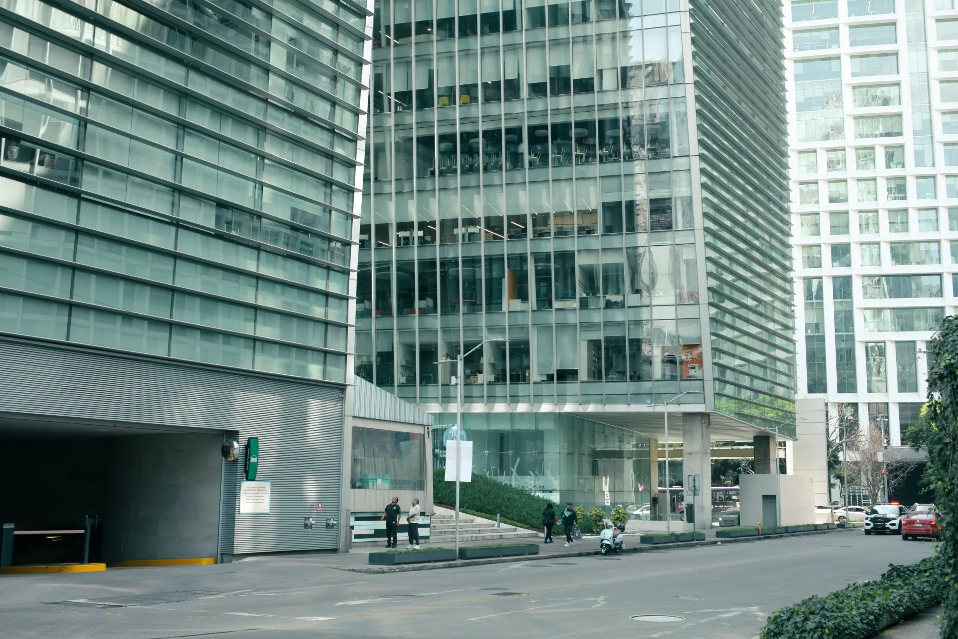 A street scene in a city with modern glass buildings, people walking, and park vehicles.