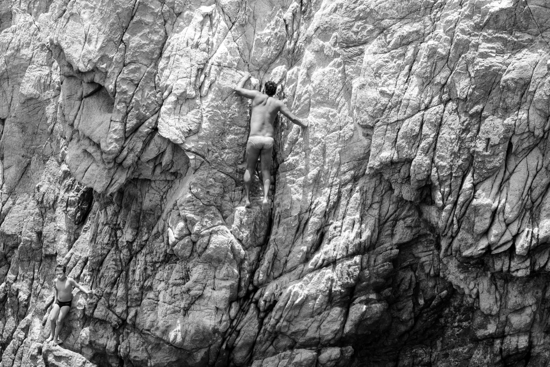 Two young men rock climbing on a large, textured rocky cliff outdoors.