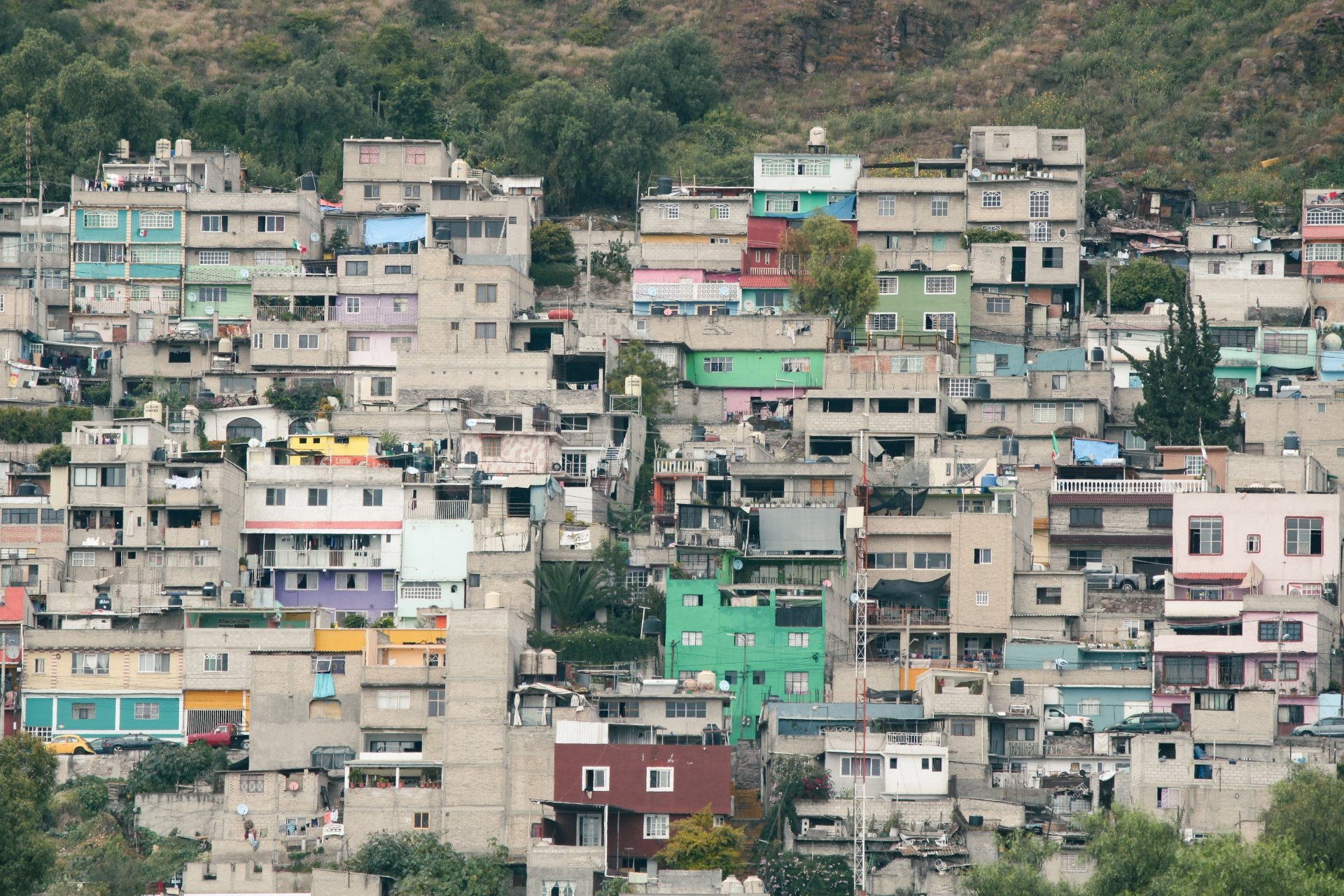 A hillside filled with closely packed, multi-colored residential buildings stacked on top of each other, with some trees and vegetation surrounding the structures.