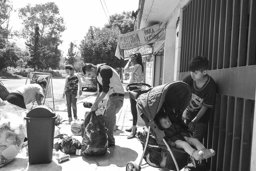 People participating in a community cleanup or donation event outside a building, with a young boy pushing a stroller with a sleeping child.