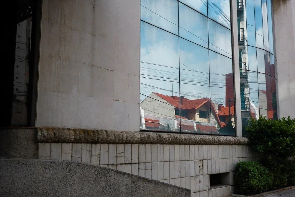 Reflection of houses with red roofs and a utility pole in a glass window of a modern building.