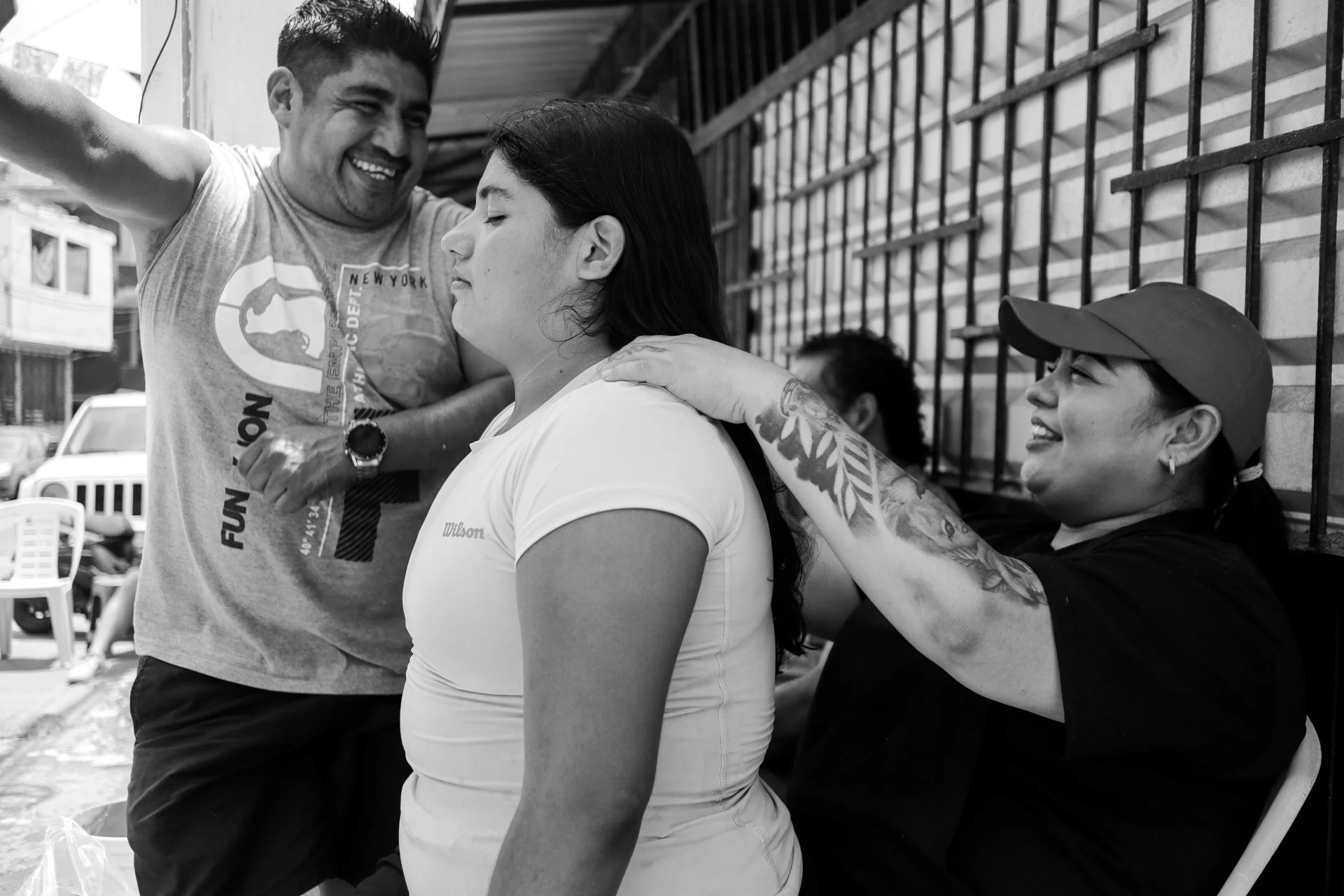 A woman with long dark hair receiving a vaccination from a medical worker, while a man beside her smiles and looks down.