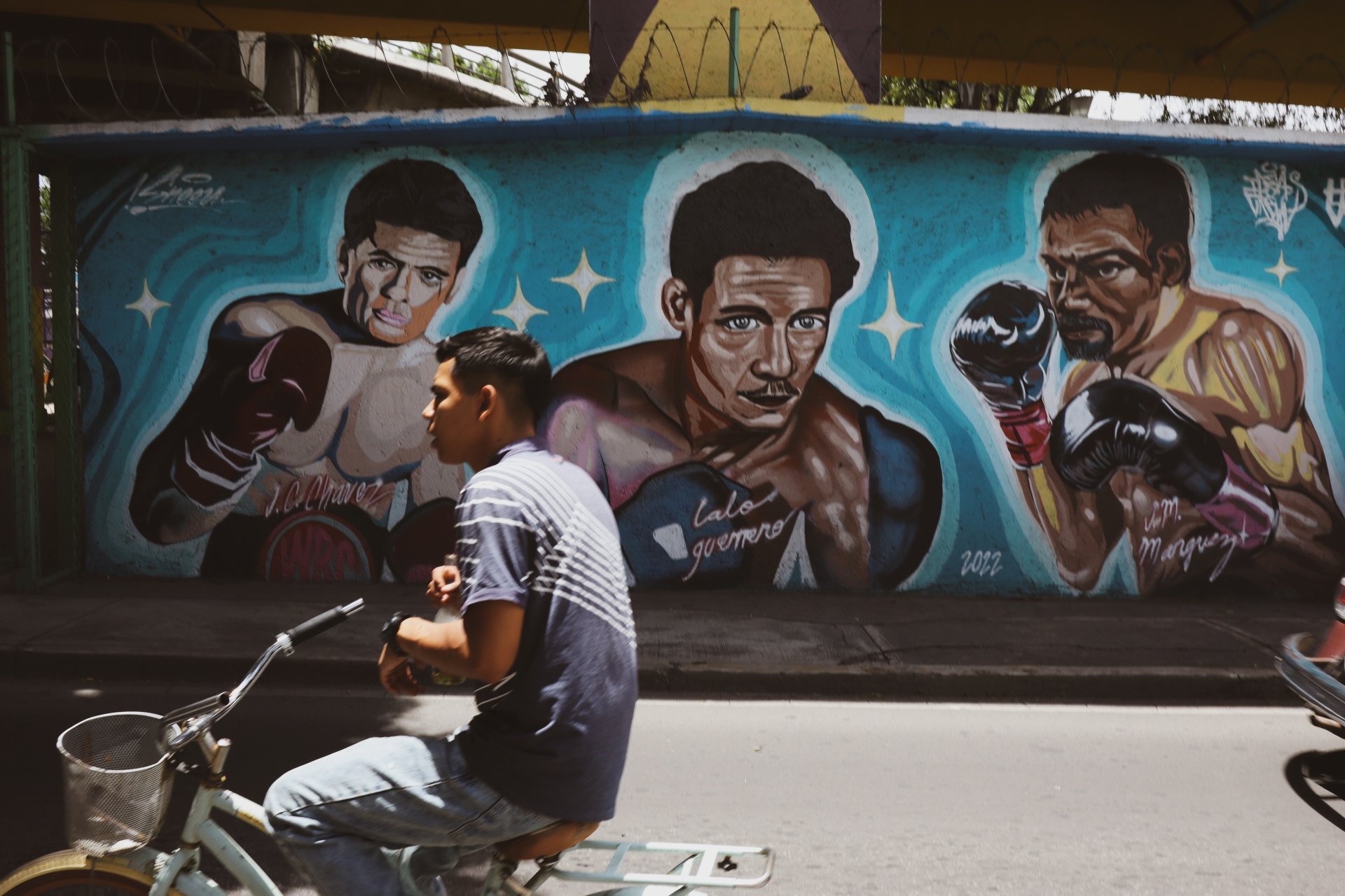 Guys in bike passing in front of boxers wall