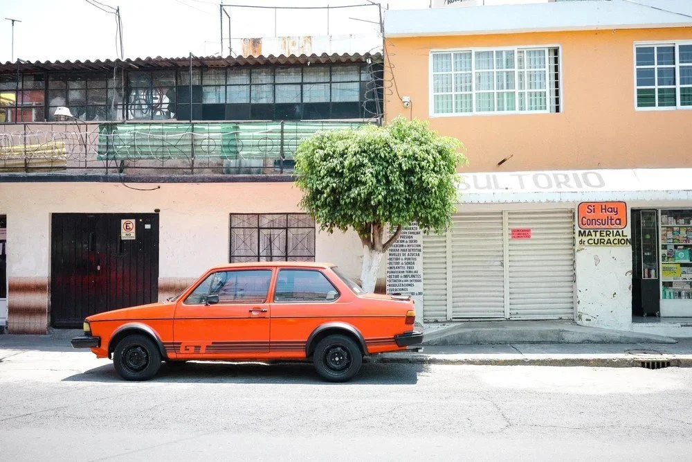 Orange vintage car parked on street in front of a building with a tree.