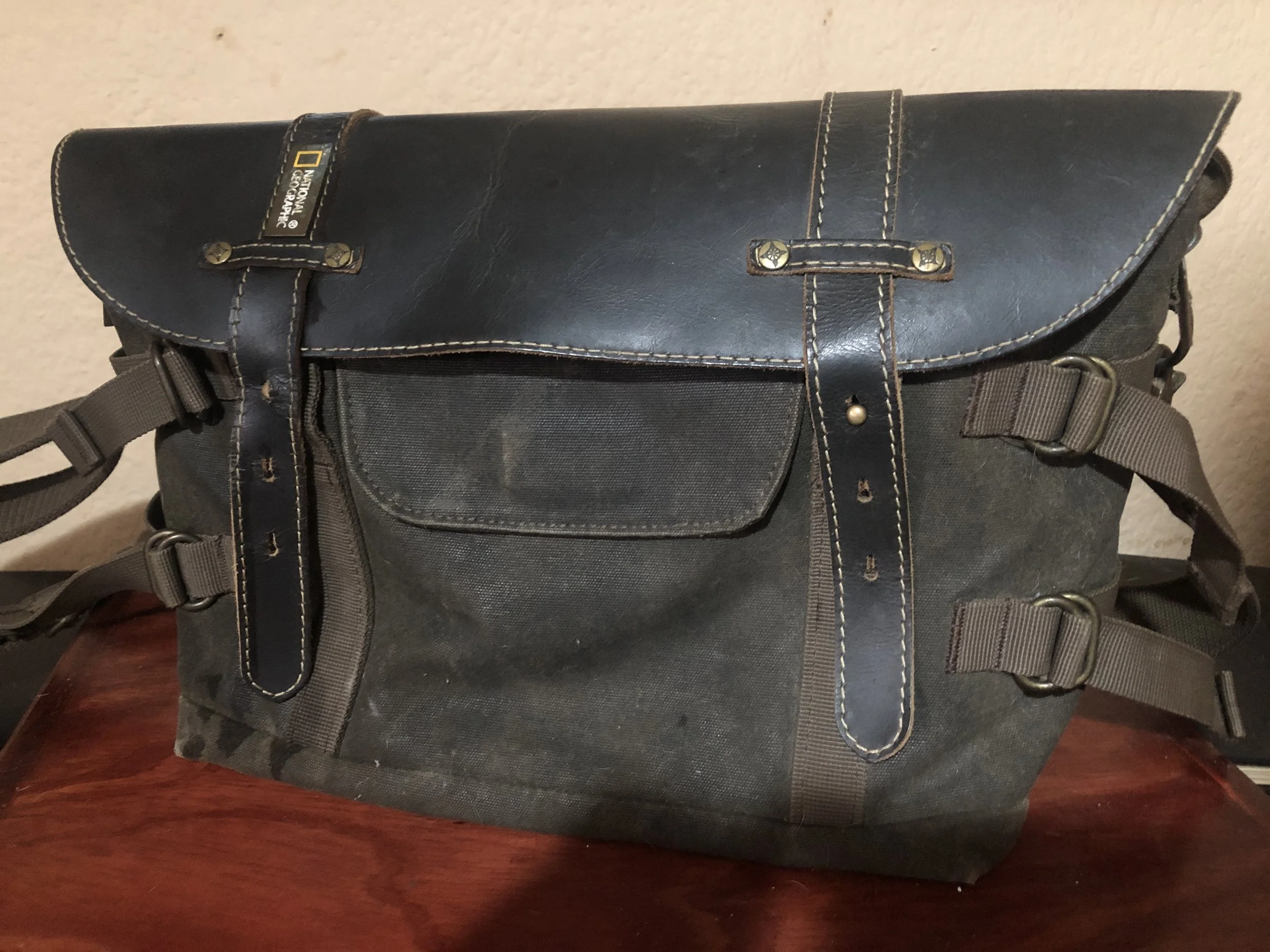 A black and gray camera bag with multiple straps and metal decorations on a wooden surface