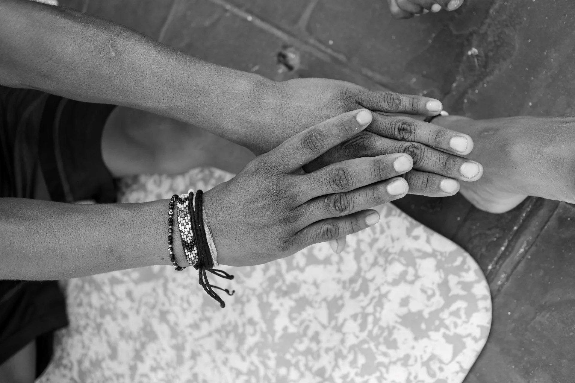 Close-up of two hands touching on a rough surface, one hand is darker-skinned, wearing bracelets, the other lighter-skinned.