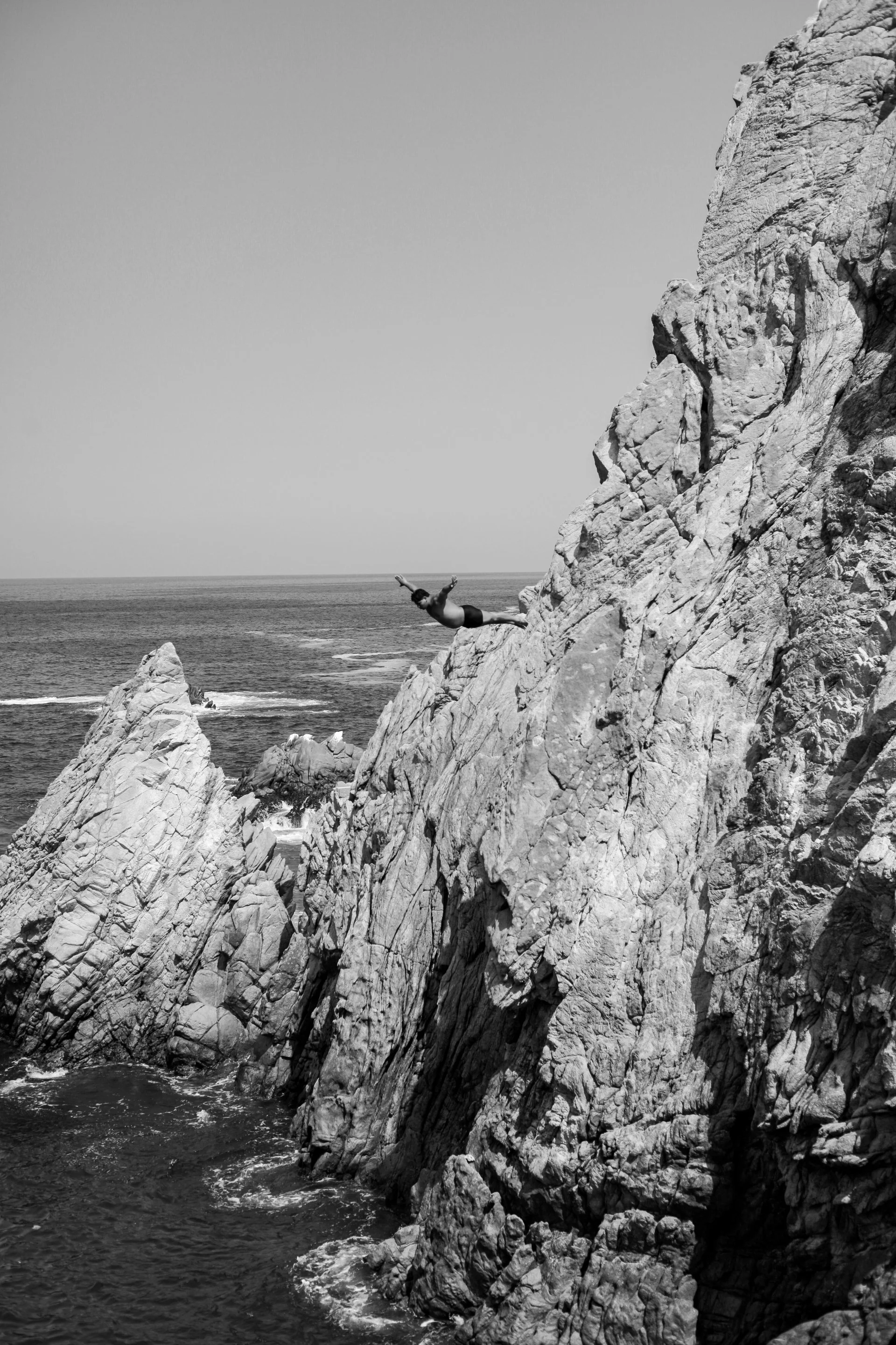 A person wearing a swimsuit bungee jumping off a large rocky cliff over the ocean.