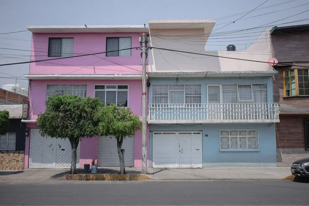 Colorful urban house with pink and blue sections, featuring windows, balconies, and trees in front.
