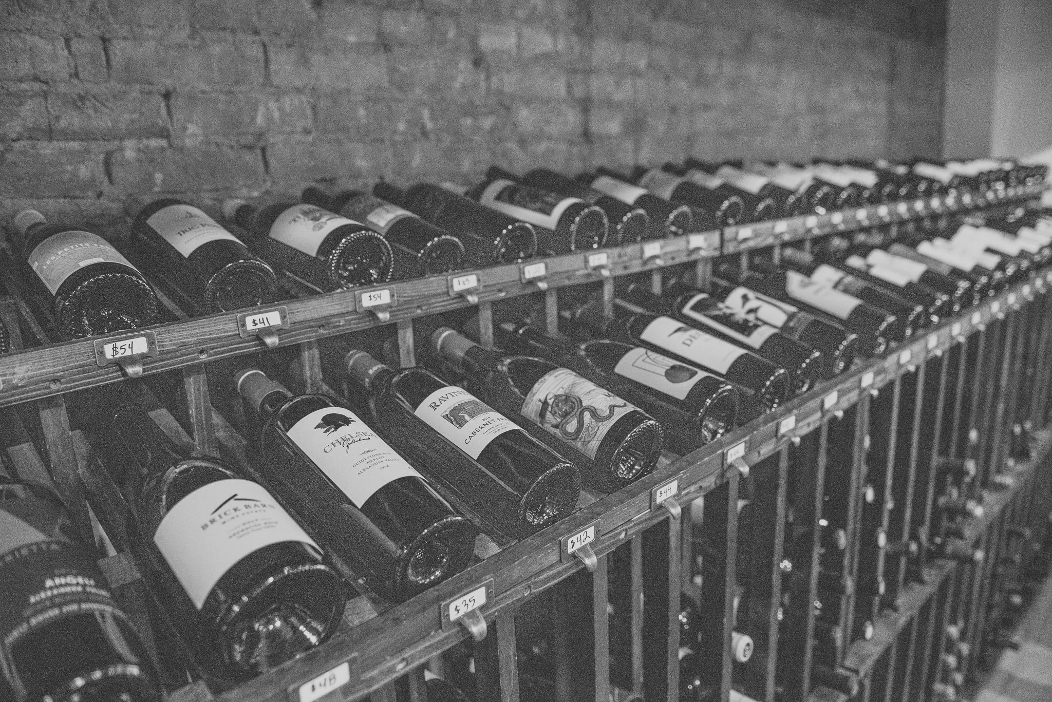 Rows of wine bottles stored on wooden racks in a wine cellar or store.