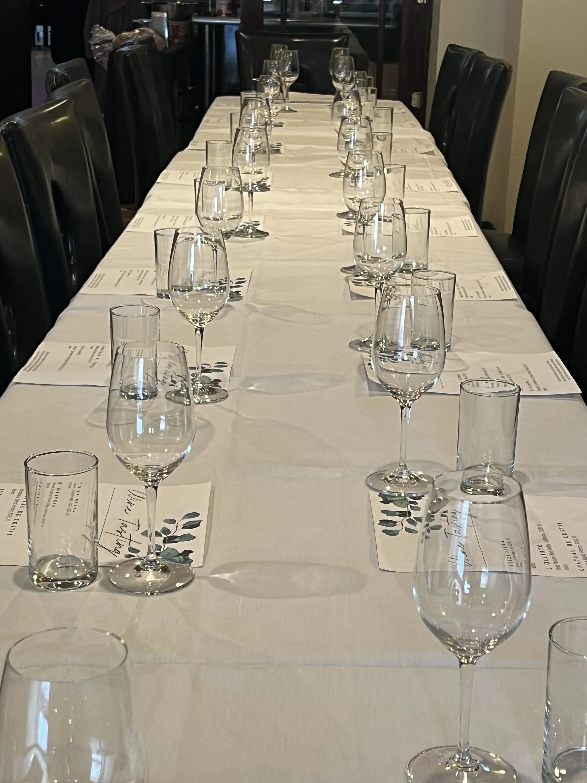 A long rectangular table set for a formal dinner with wine glasses, water glasses, and printed menus or place cards, in a dimly lit restaurant event space.