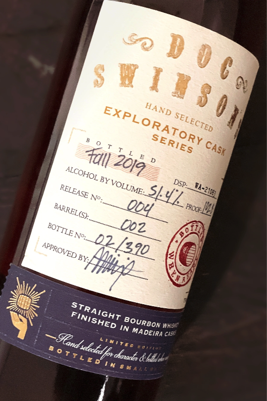Close-up of a whiskey bottle label featuring handwritten details, including 'Full 2019', 51.4% alcohol, and other bottling information, with a blue band at the bottom indicating it's a straight bourbon whiskey finished in Madeira casks.