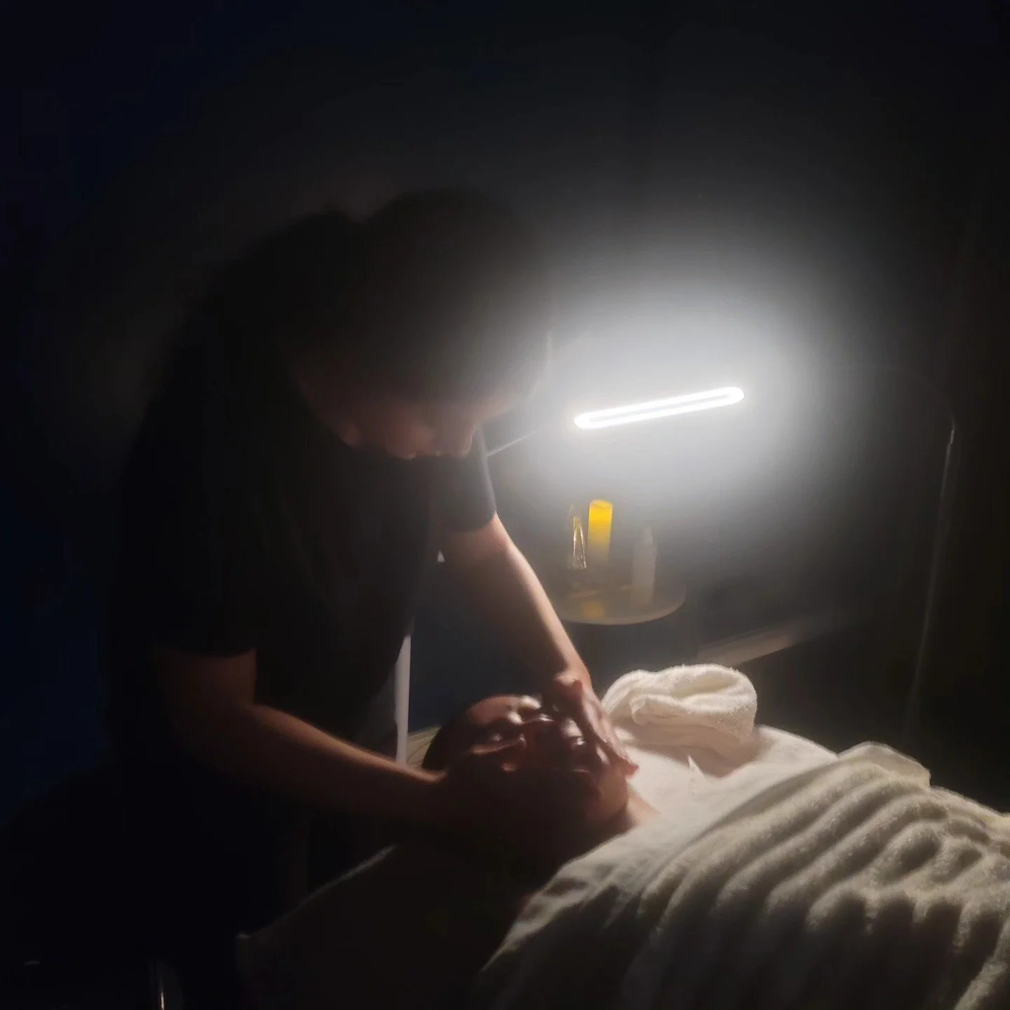 Paulina, one of our licensed estheticians standing over a client taking a facial nap as she finishes with serum and moisturizer.