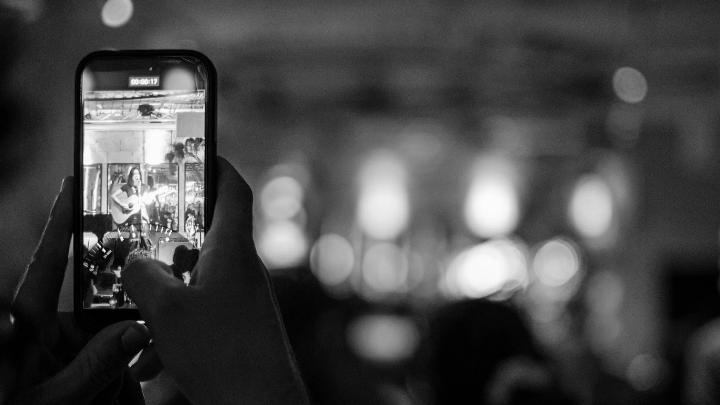 Person holding a phone capturing a live music performance in black and white.