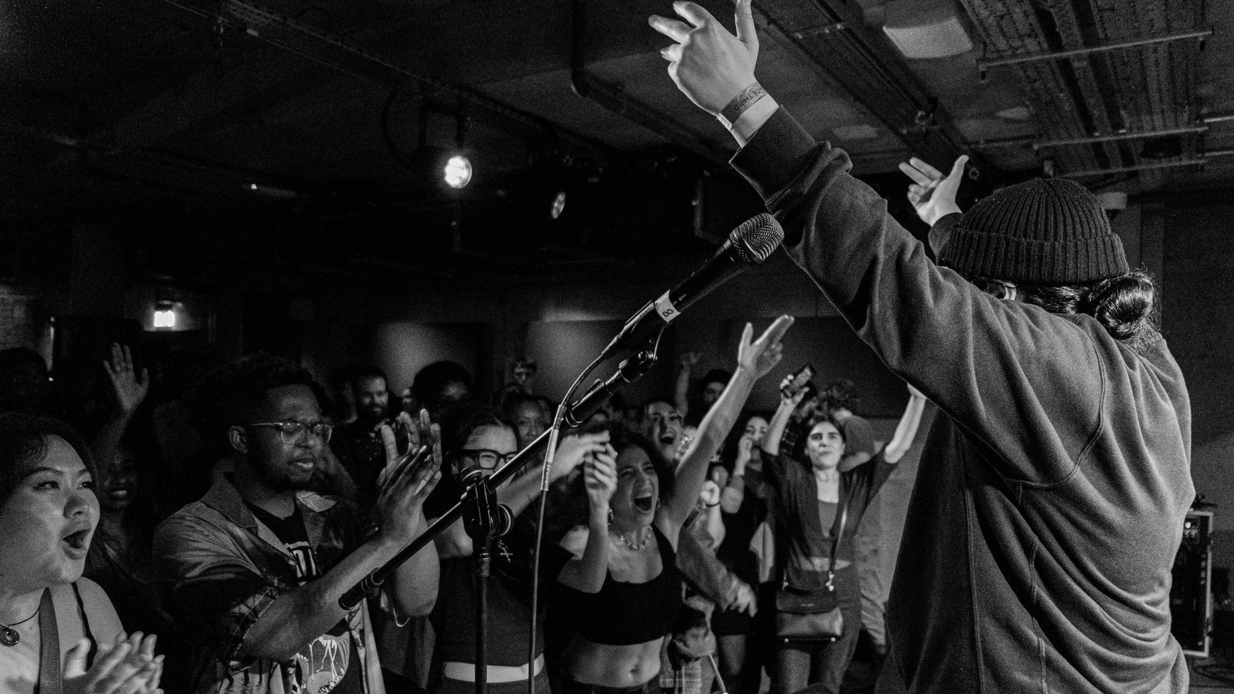 Black and white photo of a person on stage with raised hands and an excited audience.