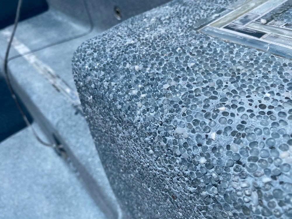 Close-up of a rounded blue-gray pebble-textured pool surface beside rectangular mosaic tile trim.