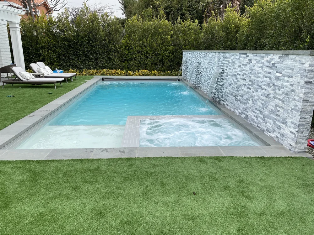 Front view of a compact pool with a wide pale shallow shelf, square spa, and tall patterned feature wall.