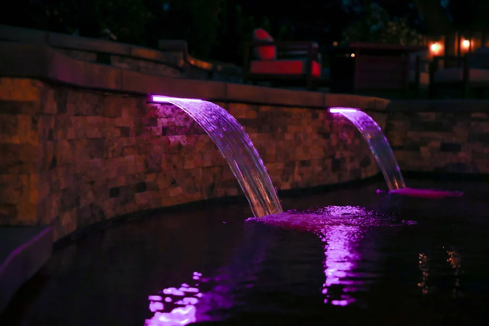Purple lighting illuminates two sheet waterfalls and their reflections in a dark pool.