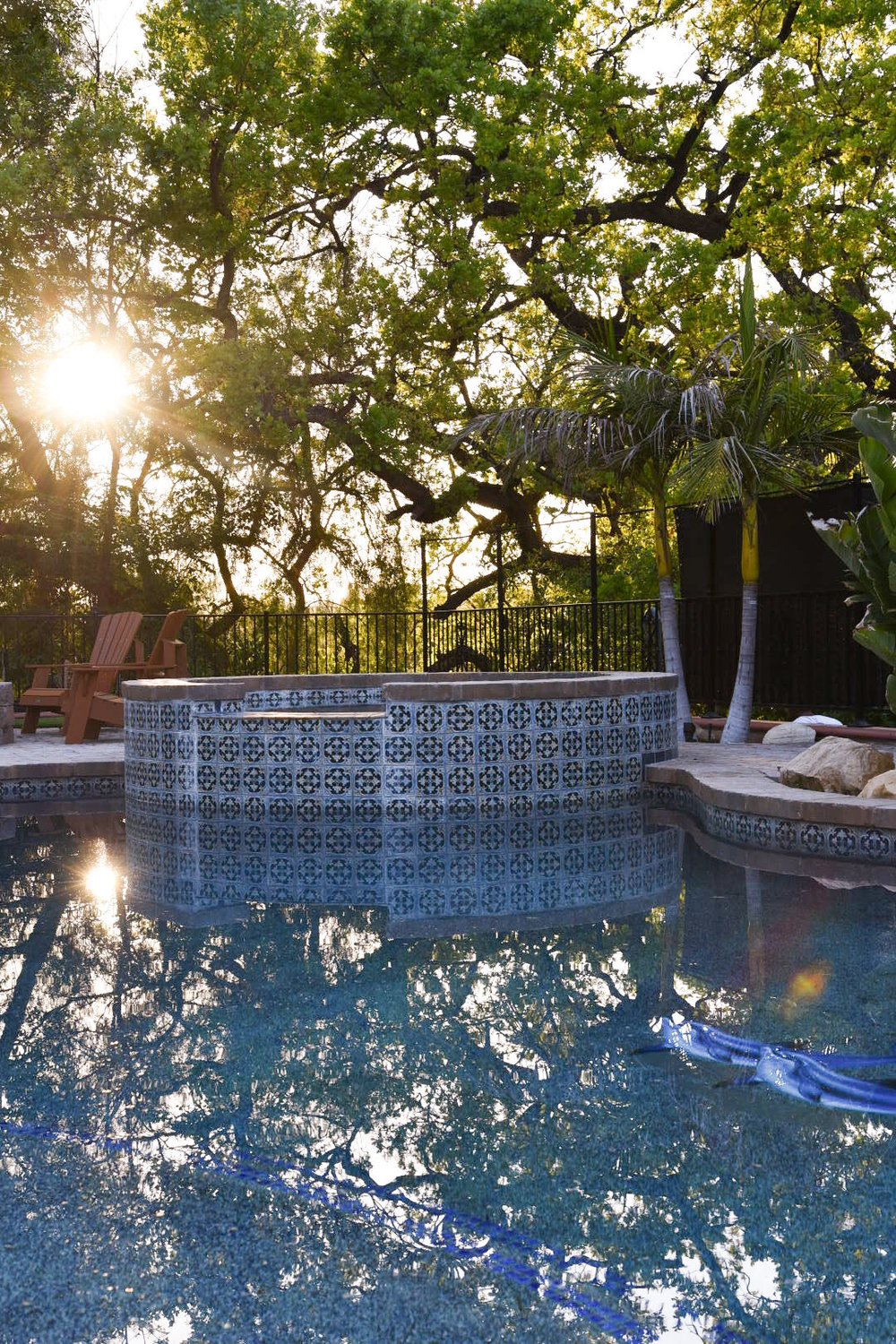 Raised round spa with blue-and-white patterned tile reflecting in the pool as sunlight filters through the trees.