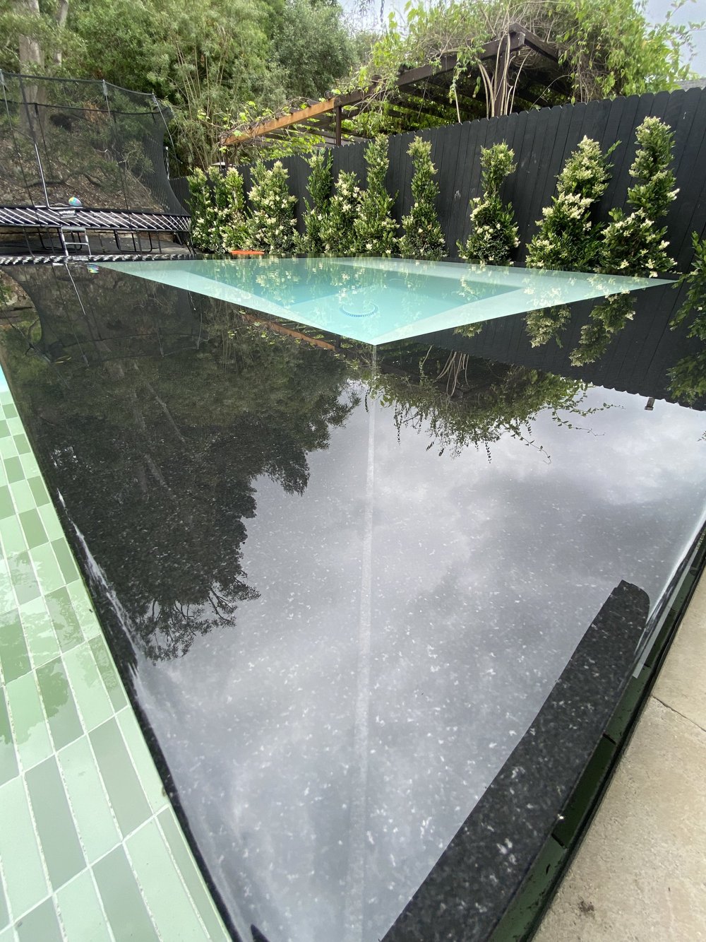 Close view of a broad reflective dark spa edge surrounding pale turquoise water, with planting reflected in its surface.